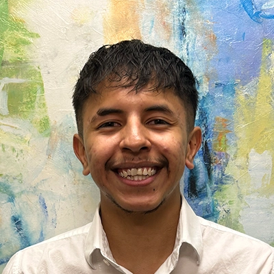 Gustavo Mosqueda-Cuellar Smiling In Front Of Watercolor Wall